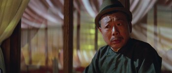 Movie still from “Miracles: The Canton Godfather” (1989), directed by Jackie Chan – An older man wearing a hat and looking at the camera; Close Up shot, Low angle