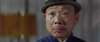 Movie still from “Miracles: The Canton Godfather” (1989), directed by Jackie Chan – An older man wearing a hat and looking at the camera; Close Up shot, Low angle