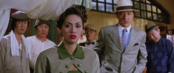 Movie still from “Miracles: The Canton Godfather” (1989), directed by Jackie Chan – A woman in a green dress and a hat; Close Up shot, Over the shoulder angle