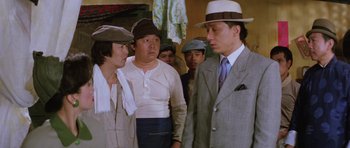 Movie still from “Miracles: The Canton Godfather” (1989), directed by Jackie Chan – A group of people standing next to each other wearing hats; Medium shot, Low angle