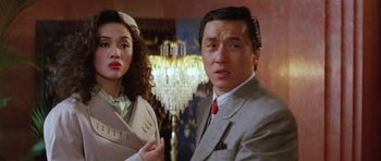 Movie still from “Miracles: The Canton Godfather” (1989), directed by Jackie Chan – A man and a woman standing next to each other in a room; Medium shot, Over the shoulder angle
