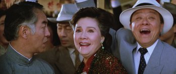 Movie still from “Miracles: The Canton Godfather” (1989), directed by Jackie Chan – An older woman smiles while sitting next to a man; Close Up shot, Low angle