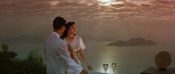 Movie still from “Miracles: The Canton Godfather” (1989), directed by Jackie Chan – A man and a woman standing next to each other near water; Medium shot, Low angle