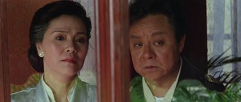 Movie still from “Miracles: The Canton Godfather” (1989), directed by Jackie Chan – An older man and a younger woman looking in the same mirror; Close Up shot, Over the shoulder angle