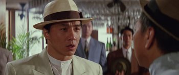 Movie still from “Miracles: The Canton Godfather” (1989), directed by Jackie Chan – A man wearing a white suit and a white hat; Close Up shot, Over the shoulder angle