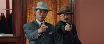 Movie still from “Miracles: The Canton Godfather” (1989), directed by Jackie Chan – A couple of men standing next to each other holding guns; Medium shot, Low angle