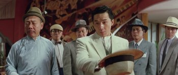 Movie still from “Miracles: The Canton Godfather” (1989), directed by Jackie Chan – A group of men standing next to each other in a room; Medium shot, Low angle