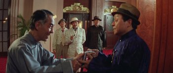 Movie still from “Miracles: The Canton Godfather” (1989), directed by Jackie Chan – A group of men standing next to each other in a room; Medium shot, Over the shoulder angle