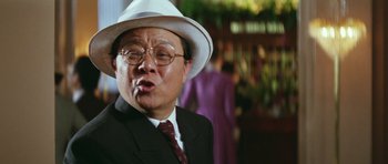 Movie still from “Miracles: The Canton Godfather” (1989), directed by Jackie Chan – An older man wearing a white hat and a suit; Close Up shot, Low angle