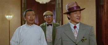 Movie still from “Miracles: The Canton Godfather” (1989), directed by Jackie Chan – A group of men standing next to each other in a hallway; Close Up shot, Over the shoulder angle