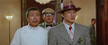 Movie still from “Miracles: The Canton Godfather” (1989), directed by Jackie Chan – A group of men standing next to each other in a room; Close Up shot, Low angle