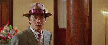 Movie still from “Miracles: The Canton Godfather” (1989), directed by Jackie Chan – A man wearing a suit and a hat in front of a wall; Close Up shot, Low angle