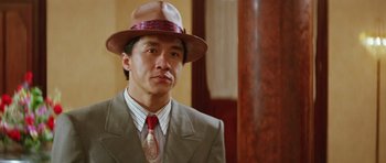 Movie still from “Miracles: The Canton Godfather” (1989), directed by Jackie Chan – A man wearing a suit and a hat and a tie; Close Up shot, Low angle