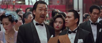 Movie still from “Miracles: The Canton Godfather” (1989), directed by Jackie Chan – A group of people standing next to each other in a room; Close Up shot, Low angle