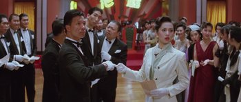 Movie still from “Miracles: The Canton Godfather” (1989), directed by Jackie Chan – A group of people standing in a room holding hands; Medium shot, Low angle
