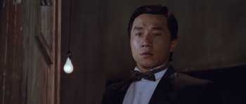 Movie still from “Miracles: The Canton Godfather” (1989), directed by Jackie Chan – A person wearing a suit and a bow tie; Close Up shot, Low angle