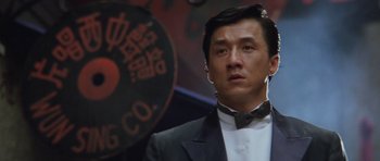 Movie still from “Miracles: The Canton Godfather” (1989), directed by Jackie Chan – A person wearing a suit and bow tie; Close Up shot, Low angle