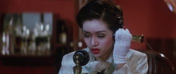 Movie still from “Miracles: The Canton Godfather” (1989), directed by Jackie Chan – A woman in a white dress talking on a phone; Close Up shot, High angle