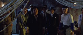 Movie still from “Miracles: The Canton Godfather” (1989), directed by Jackie Chan – A group of men standing next to each other wearing suits and hats; Medium shot, Low angle