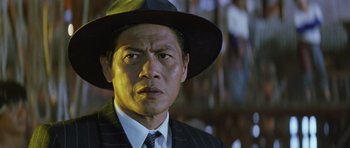 Movie still from “Miracles: The Canton Godfather” (1989), directed by Jackie Chan – A person wearing a suit and a hat; Close Up shot, Low angle