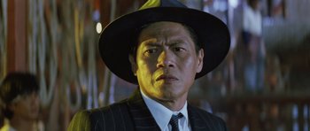 Movie still from “Miracles: The Canton Godfather” (1989), directed by Jackie Chan – A person wearing a suit and a hat; Close Up shot, Low angle