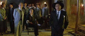 Movie still from “Miracles: The Canton Godfather” (1989), directed by Jackie Chan – A group of men in suits and hats standing in a room; Medium shot, Low angle