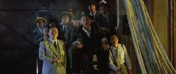 Movie still from “Miracles: The Canton Godfather” (1989), directed by Jackie Chan – A group of men in suits and hats sitting on a chair; Wide shot, Low angle