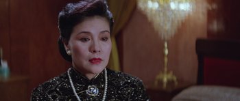 Movie still from “Miracles: The Canton Godfather” (1989), directed by Jackie Chan – An older woman wearing a black dress and a pearl necklace; Close Up shot, Over the shoulder angle