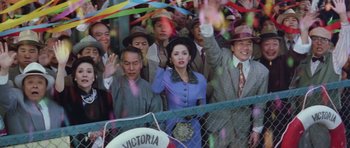 Movie still from “Miracles: The Canton Godfather” (1989), directed by Jackie Chan – A group of people standing next to each other in front of a chain link fence; Medium shot, High angle