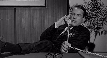 Movie still from “Mirage” (1965), directed by Edward Dmytryk – A man sitting on the ground talking on a phone; Medium shot, Low angle