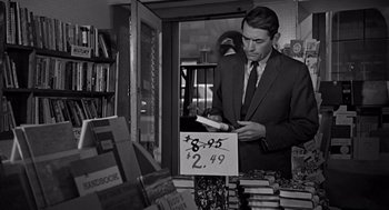 Movie still from “Mirage” (1965), directed by Edward Dmytryk – A black and white photo of a man looking at books; Medium shot, Over the shoulder angle