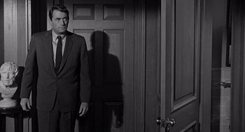 Movie still from “Mirage” (1965), directed by Edward Dmytryk – A black and white photo of a man standing in front of an open door; Medium shot, Over the shoulder angle