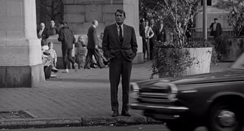 Movie still from “Mirage” (1965), directed by Edward Dmytryk – Black and white photograph of a man on a street corner; Wide shot, Over the shoulder angle