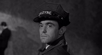 Movie still from “Mirage” (1965), directed by Edward Dmytryk – A black and white photo of a man wearing a uniform; Close Up shot, Low angle