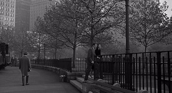 Movie still from “Mirage” (1965), directed by Edward Dmytryk – A man in a suit and tie walking on a bench next to a woman; Wide shot, Low angle
