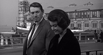 Movie still from “Mirage” (1965), directed by Edward Dmytryk – An older man standing next to an older woman; Medium shot, Low angle