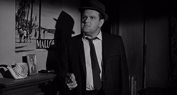 Movie still from “Mirage” (1965), directed by Edward Dmytryk – A black and white photo of a man holding a gun; Medium shot, Low angle