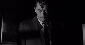Movie still from “Mirage” (1965), directed by Edward Dmytryk – Black and white photograph of a man wearing a suit and tie; Close Up shot, Over the shoulder angle