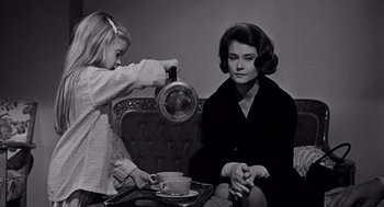 Movie still from “Mirage” (1965), directed by Edward Dmytryk – A woman sitting on a chair holding a tea pot while a little girl stands next to her holding a tray; Medium shot, High angle