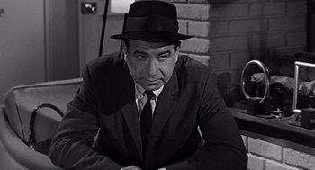 Movie still from “Mirage” (1965), directed by Edward Dmytryk – Black and white photograph of a man wearing a suit and a hat; Close Up shot, High angle