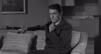 Movie still from “Mirage” (1965), directed by Edward Dmytryk – Black and white photograph of a man sitting on a couch; Medium shot, High angle