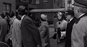 Movie still from “Mirage” (1965), directed by Edward Dmytryk – An old black and white photo of people walking down the street; Medium shot, Over the shoulder angle