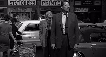 Movie still from “Mirage” (1965), directed by Edward Dmytryk – Two men in suits and ties standing next to each other in front of cars; Medium shot, Low angle