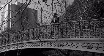 Movie still from “Mirage” (1965), directed by Edward Dmytryk – A man standing on top of a metal bridge near trees; Wide shot, Low angle