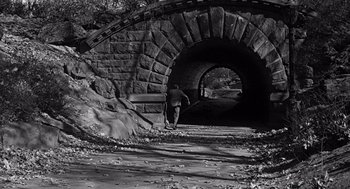 Movie still from “Mirage” (1965), directed by Edward Dmytryk – A man walking down a path under a bridge; Wide shot, High angle