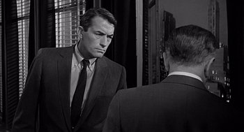 Movie still from “Mirage” (1965), directed by Edward Dmytryk – A black and white photo of a man in a suit looking at himself in the mirror; Medium shot, Over the shoulder angle