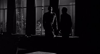 Movie still from “Mirage” (1965), directed by Edward Dmytryk – Two men are standing in front of a large window; Wide shot, Low angle
