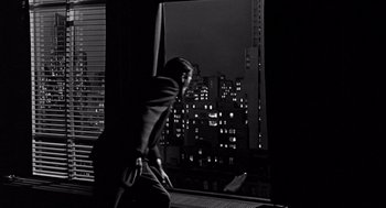 Movie still from “Mirage” (1965), directed by Edward Dmytryk – A black and white photo of a man looking out of a window at night; Wide shot, Low angle