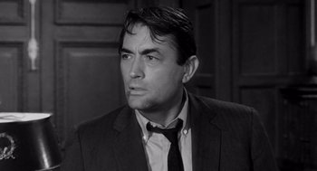 Movie still from “Mirage” (1965), directed by Edward Dmytryk – Black and white photograph of a man wearing a suit and tie; Close Up shot, Over the shoulder angle