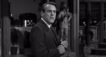 Movie still from “Mirage” (1965), directed by Edward Dmytryk – Black and white photograph of a man wearing a suit and tie; Medium shot, Low angle